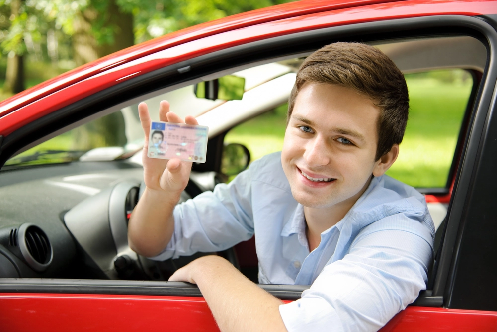 Jongere laat zijn rijbewijs zien vanuit de auto, lachend
